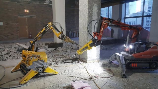 To rivningsroboter i arbeid innendørs i et bygg under renovering.